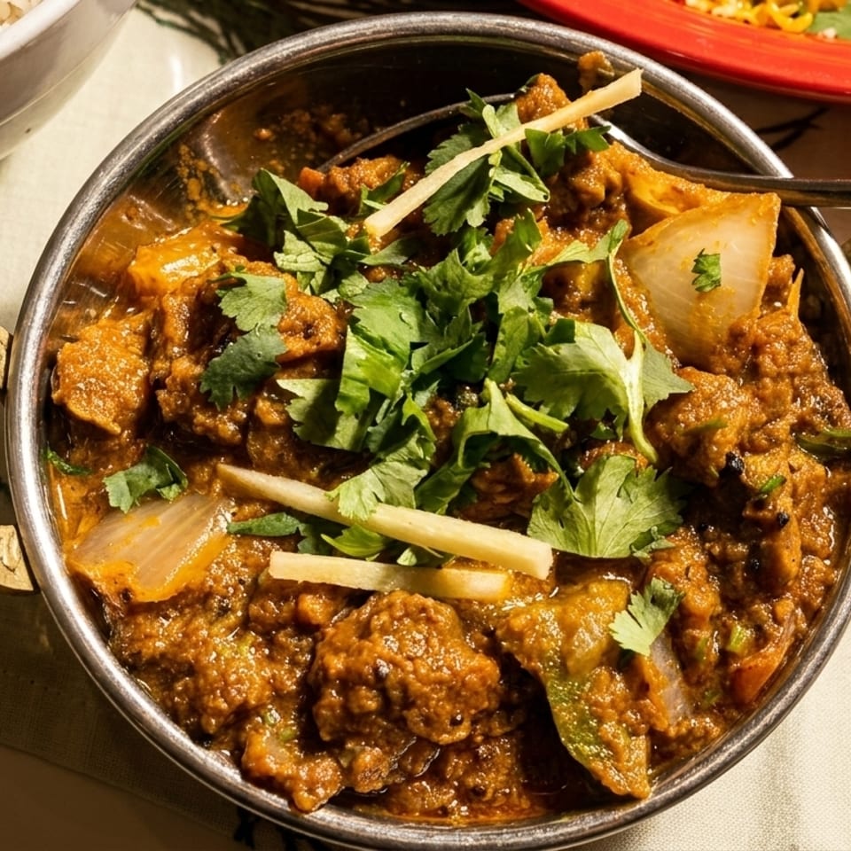 Close-up of a metal bowl filled with Indian curry, garnished with cilantro and ginger.