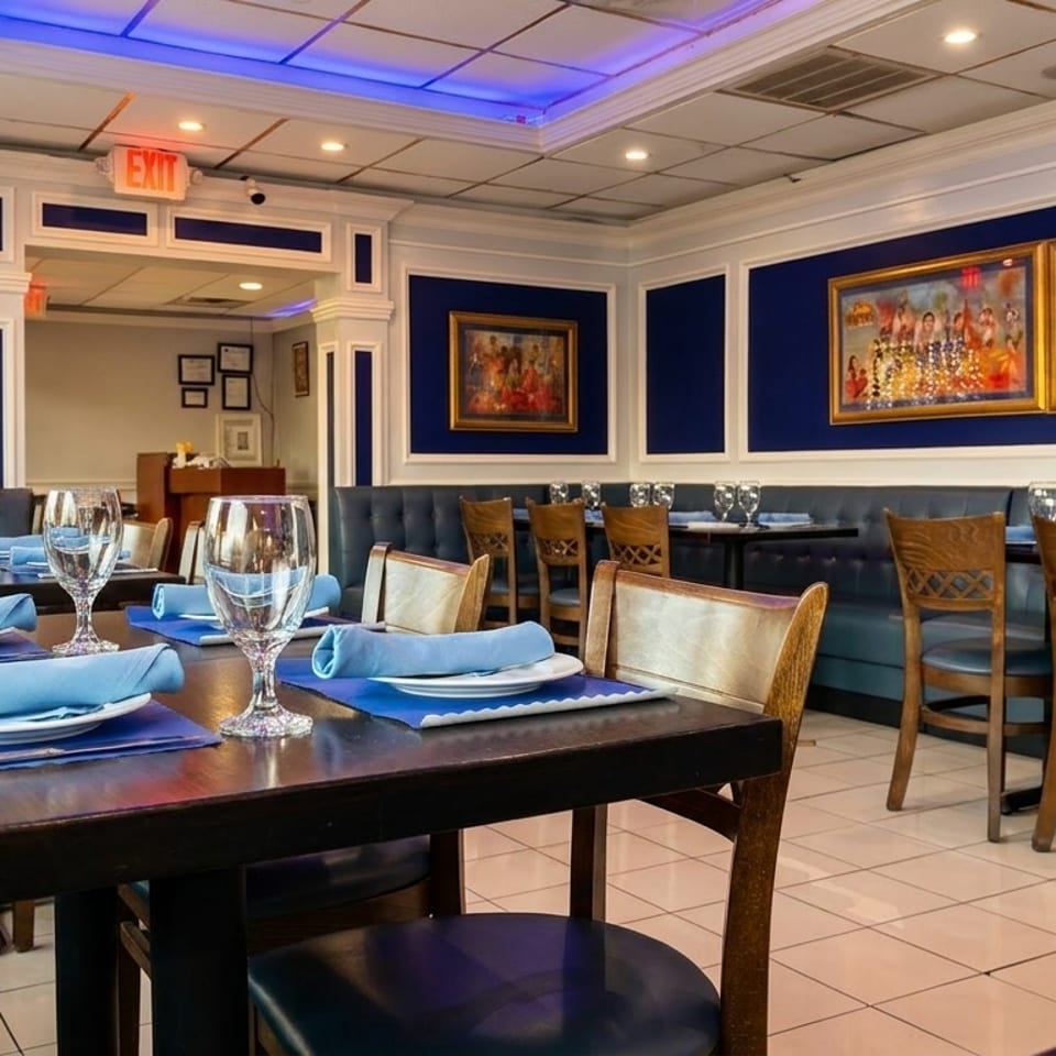 Restaurant interior with blue booths, wooden chairs, set tables, and framed artwork on blue walls.