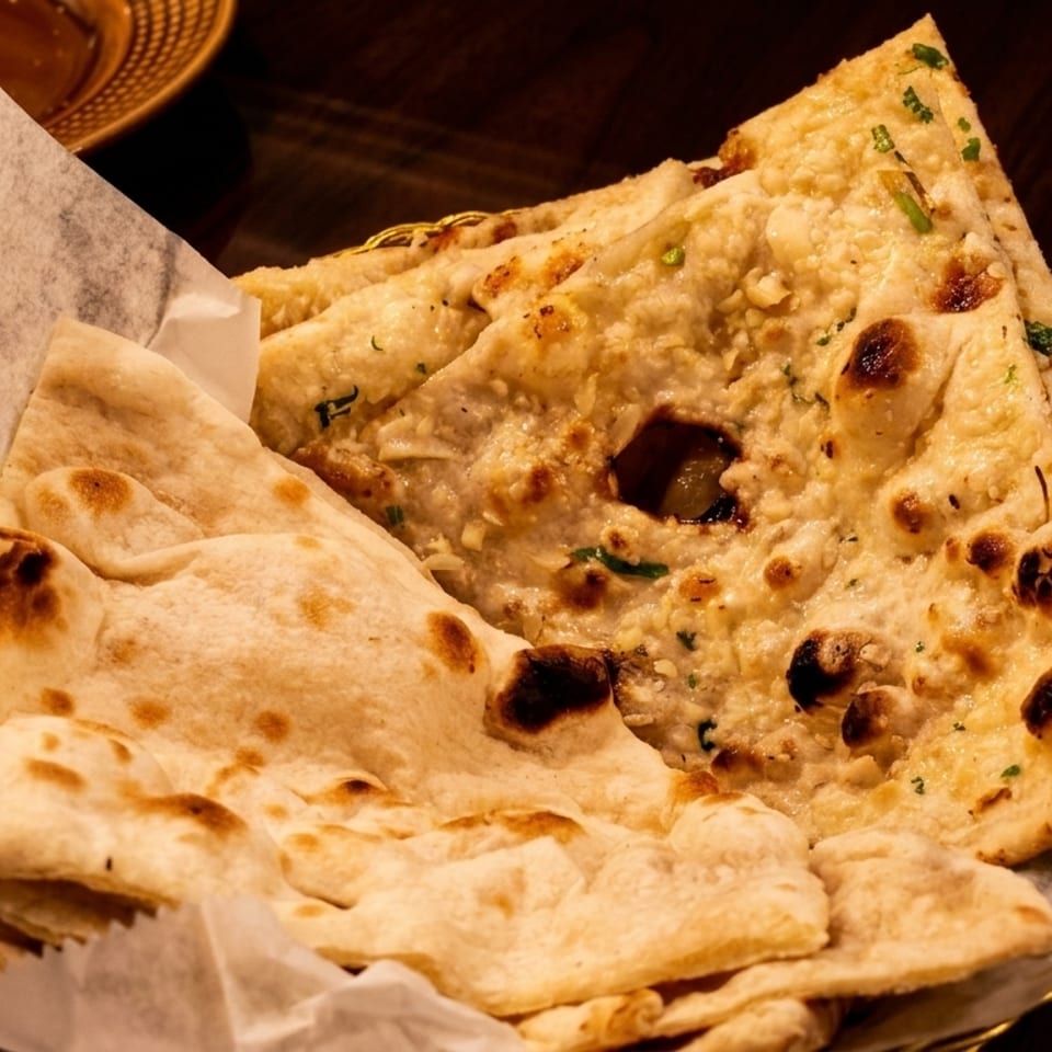 Basket of freshly baked naan bread, some plain and some garlic, with dipping sauces in the background.