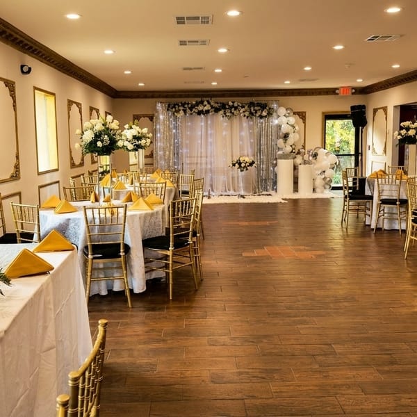 Elegant event hall with round tables, gold chairs, white floral centerpieces, and a sparkling backdrop.